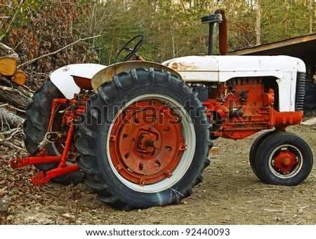 A high contrast shot of an old large orange and antique white Farm Tractor in the woods.
