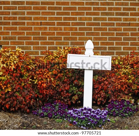 A small white cross among the spring flowers and foliage against a brick wall with room for your text.