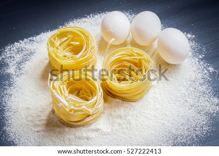 Eggs, flour and fettuccine on a gray background.