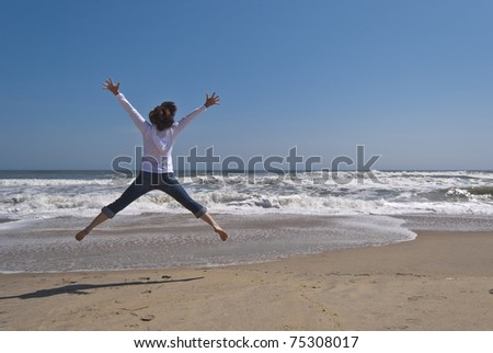 Attractive woman in her 40s is jumping for joy on a secluded beach. Image was taken at the Outer Banks in North Carolina