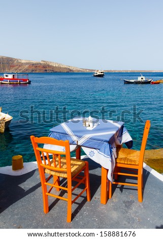 Table and chairs in front of the sea with blue sea and sky as a background in Ammoudi, Santorini, Grecee