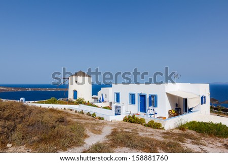 View of the windmill near a small traditional villa against a blue sky in Oia, Santorini, Greece