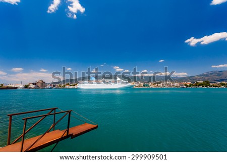 Big cruise ship anchored in port against a blue sky and clouds with rusty embarking platform in the foreground in Greece