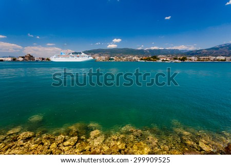 Big cruise ship anchored in port with turquoise waters in the foreground against a blue sky and clouds in Greece