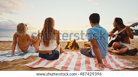 Group of friends relaxing around bonfire on the beach at sunset