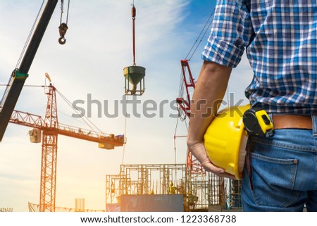 Construction \
architect or engineer or worker or foreman holding safety yellow  helmet(hard hat) and \
Measuring Tapestanding in construction site.Construction Engineering,foreman and worker concept.