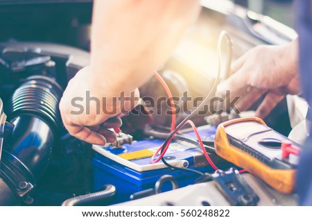 Selective focus an auto mechanic uses a multimeter voltmeter to check the voltage level in a car battery.