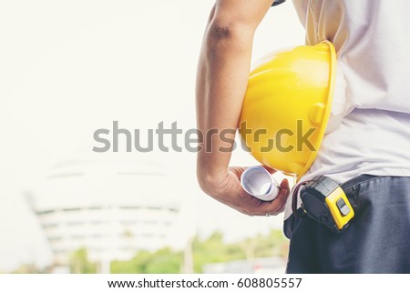 Close up back view of male construction worker holding roll of drawing and safety helmet outdoor of construction site.copy space.