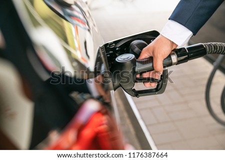 A businessman in a suit manages his car with gasoline at a gas station. Hand and black refueling gun close-up.