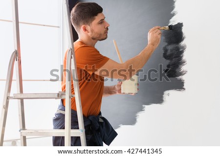 Man paints the wall in black standing on a stepladder.