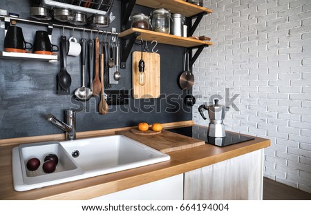 Design of a modern home kitchen in the attic and rustic style. Black wall with shelves, trays, jars, mugs, sink. In the background a wall of white brick.