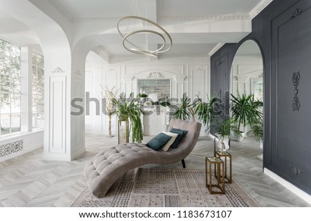 Morning in luxurious light interior in hotel. Bright and clean interior design of a luxury living room with parquet wood floors, fireplace, sofa and houseplant. Stucco on walls