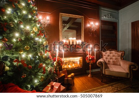 Christmas evening by candlelight. classic apartments with a white fireplace, decorated tree, sofa, large windows and chandelier.