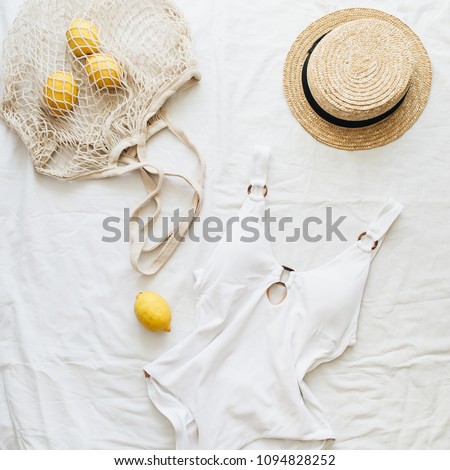 Summer travel fashion composition. Women\'s swimsuit, straw and lemons in string bag on linen background. Flat lay, top view minimal clothes concept.