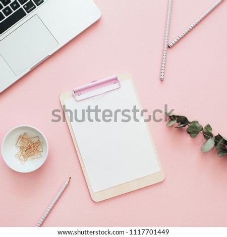 Flat lay office workspace with blank laptop, clipboard, eucalyptus branches on pink background. Top view minimal mock up template concept.