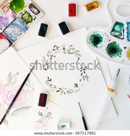 Workspace. Wreath frame with flowers and leaves painted with watercolor and paintbrush isolated on white background. Overhead view. Flat lay, top view