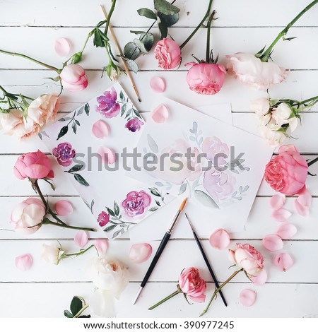 Workspace. Pink and red roses painted with watercolor, paintbrush and roses on white wooden background. Overhead view. Flat lay