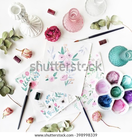 Workspace. Pink and red roses painted with watercolor, paintbrush and roses on white wooden background. Overhead view. Flat lay, top view