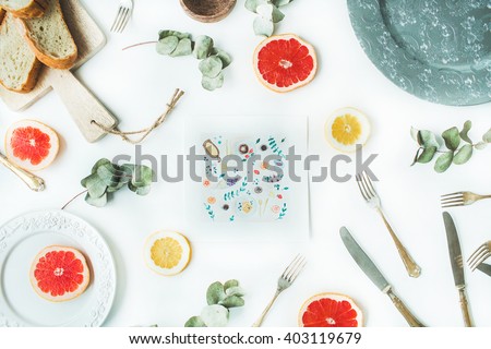 Workspace. Food plate painted with watercolor on paper, bread on cutting board, oranges, green leaves, lemon, knife, fork and plate isolated on white background. Flat lay, overhead view, top view