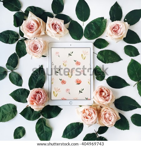 Tablet and pink rose flower with green leaves on white background. Top view, flat lay