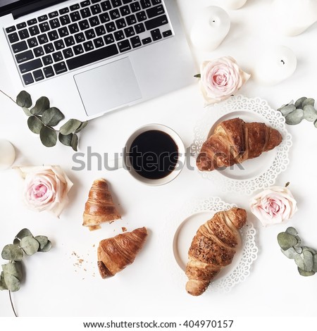 Coffee break with laptop, croissants, pink rose flower, petals, candles, vintage plates and black coffee composition. Flat lay, top view