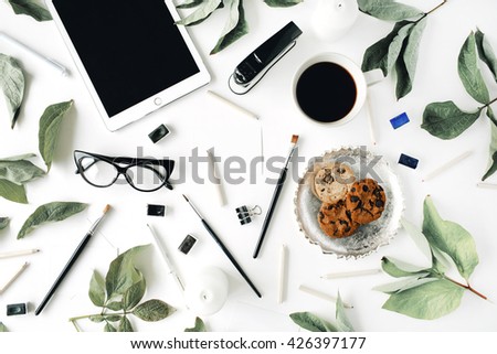 Workspace with tablet, glasses, cup of black coffee, cookies on golden tray, pencils, paintbrushes and leaf. Flat lay composition for bloggers, magazines, social media and artists. Top view.