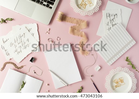Flat lay, top view office table desk. feminine desk workspace with laptop, diary, spool with ribbon, calligraphy quotes and golden clips on pink background.