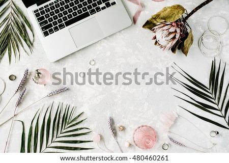 flat lay feminine home office workspace with laptop, proteus flower, necklace, palm branches and accessories. top view