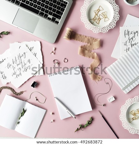 Flat lay, top view office table desk. feminine desk workspace with laptop, diary, spool with ribbon, calligraphy quotes and golden clips on pink background.