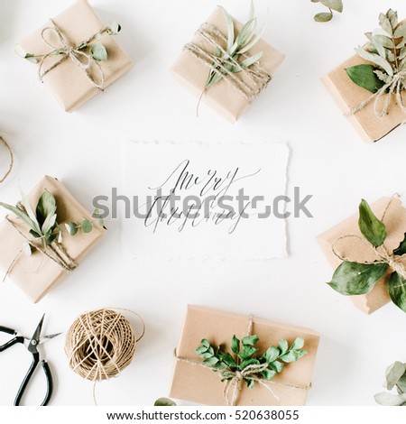calligraphy words merry christmas and beauty arrangement frame of craft boxes and green branches on white background. flat lay, top view