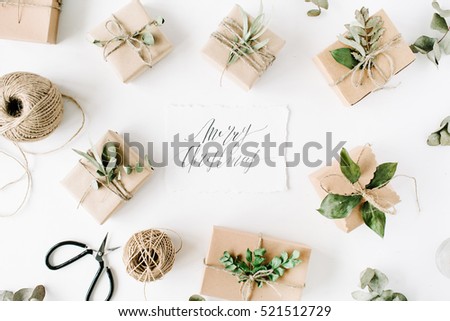 calligraphy words merry christmas and beauty arrangement frame of craft boxes and green branches on white background. flat lay, top view