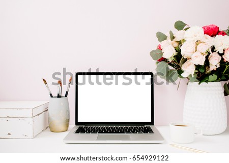 Home office desk with blank screen laptop, beautiful roses and eucalyptus bouquet, white vintage casket in front of pale pastel pink background. Blog, website or social media concept .
