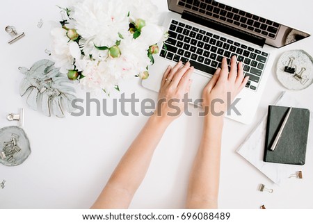 Flat lay home office desk. Women workspace with female hands, laptop, white peony flowers bouquet, accessories, marble diary. Top view feminine background. Girl working on laptop.