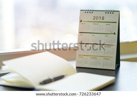 Notebook diary is on table for writing with Calendar 2018 at Workplace Collaboration office. Planner checking schedule, agenda of event for 2018 and Marketing Promotion. Calendar 2018 Concept