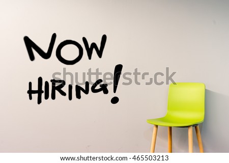 Job recruiting advertisement represented by 'NOW HIRING' texts on the  wall. The single chair is used to represent the hiring position to be recruited and filled.