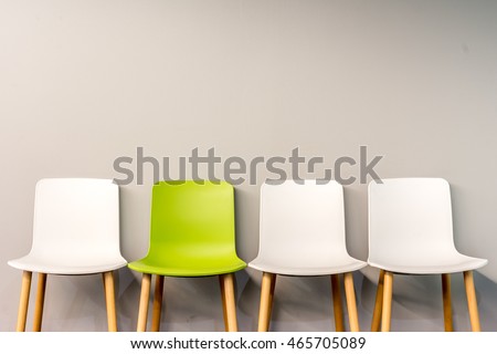 Chairs in modern design arranged in front of the gradient grey wall for interior or graphic backgrounds. The chair in different color can be used as a metaphor to represent the hiring position.
