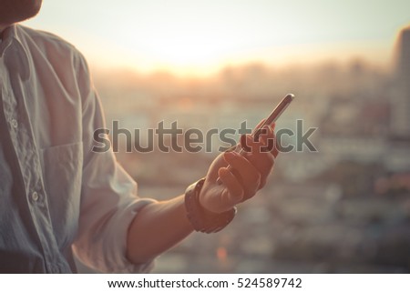 business man using a touch screen smart phone hands in sunset sky on blurred urban city as background, vintage colors