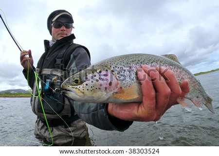 A fly fisher holds a beautiful rainbow trout in Alaska