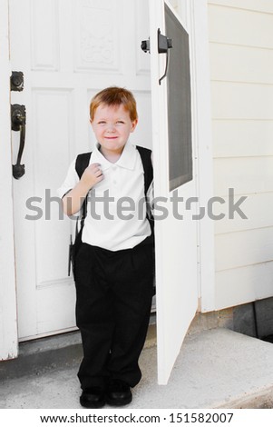 Little boy ready for school stands by the door of the house