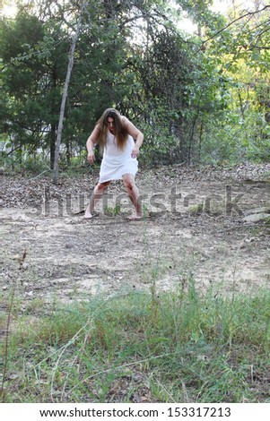 A woman in a white gown, possibly a zombie, wonders in a forest