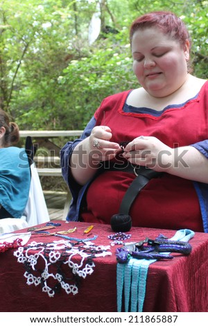 MUSKOGEE, OK - MAY 24: Woman dressed in vintage clothes works on a vintage textile craft at the Oklahoma 19th annual Renaissance Festival on May 24, 2014 at the Castle of Muskogee in Muskogee, OK