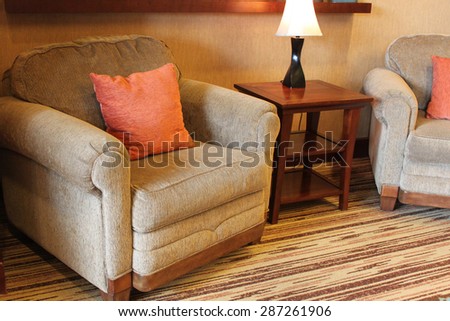 A comfy armchair with orange pillow near a small table