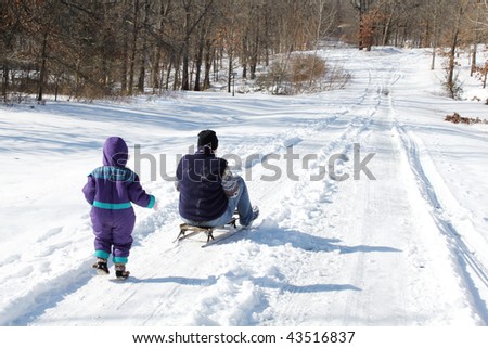 Mother rides a sled, as a child running behind it