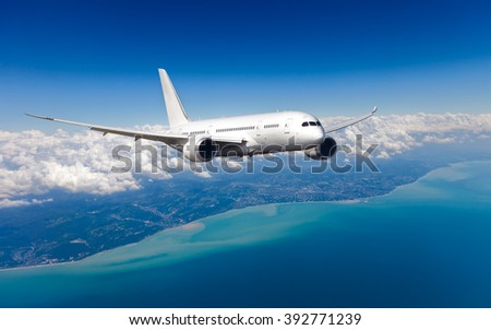 White passenger wide-body plane. Aircraft is flying in blue cloudy sky over the sea.