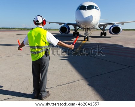 Ground Crew in the signal vest. Aviation Marshall / Supervisor meets passenger airplane at the airport. Aircraft is taxiing to the parking place.