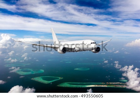 White passenger wide-body Dreamliner plane in flight. Aircraft is flying in blue cloudy sky over the sea and Maldivian islands and atolls.