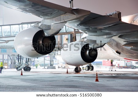 Airplane in preflight service during the winter night. Aircraft is parked at airport terminal near boarding bridge. Wing and engines of modern passenger jet plane. Close-up back view.
