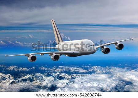 White double decker passenger plane in the blue sky. Aircraft flies high over the clouds and snow-covered mountain landscape. Airplane front view.