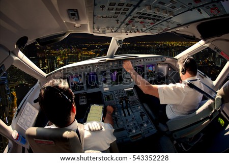 Flight Deck of modern passenger jet aircraft. Pilots at work. Night city view from the plane cockpit.