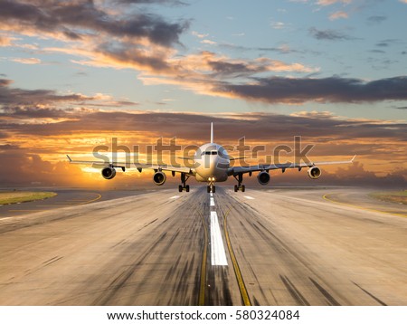 White passenger plane takes off from the airport runway. Aircraft moves against the backdrop of sunset sky. Airplane front view.